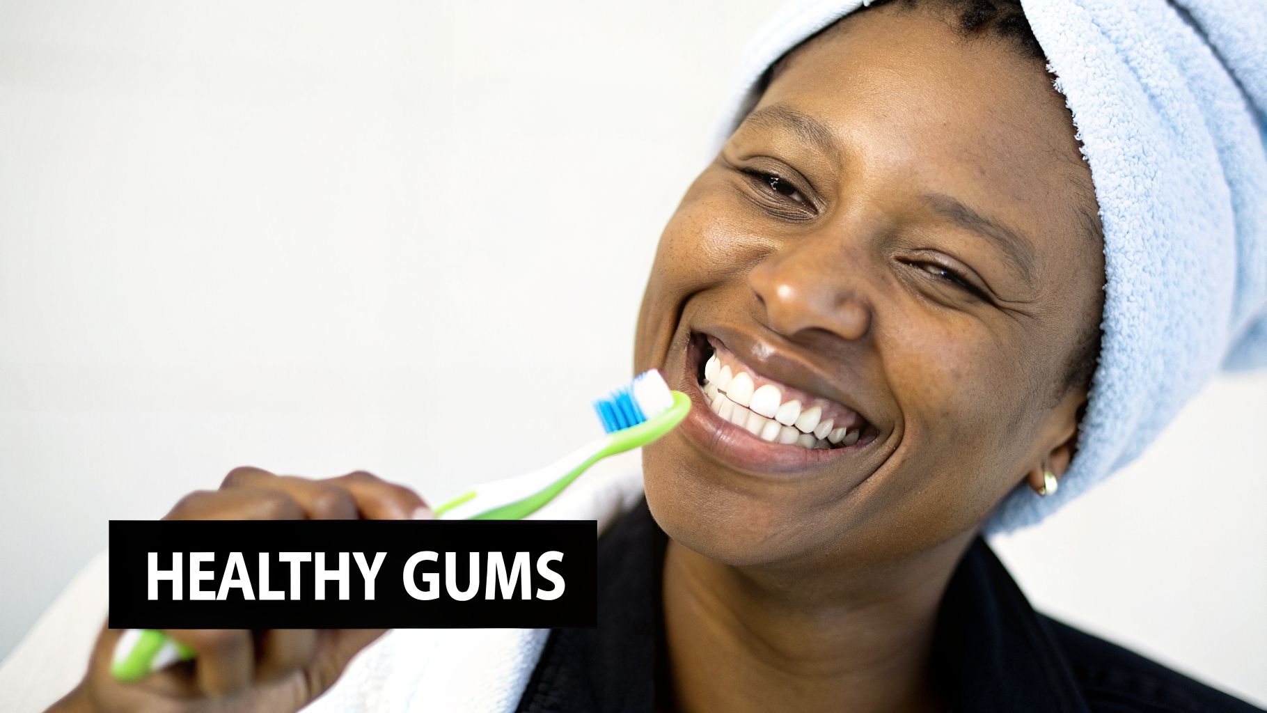 A smiling person with a light blue towel on her head brushes her teeth.